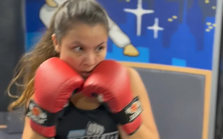 Aluna de boxe em posição de guarda com luvas vermelhas na Arena ProFight